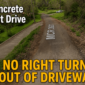 #image_title Driveway leads to a dirt road with bold yellow text at bottom: 'NO RIGHT TURN OUT OF DRIVEWAY' over greenery and trees.