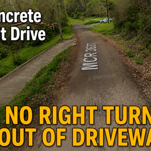 #image_title Driveway leads to a dirt road with bold yellow text at bottom: 'NO RIGHT TURN OUT OF DRIVEWAY' over greenery and trees.