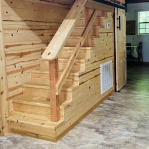 #image_title Wooden staircase to a loft inside a rustic room, with pale wood panel walls and railing.