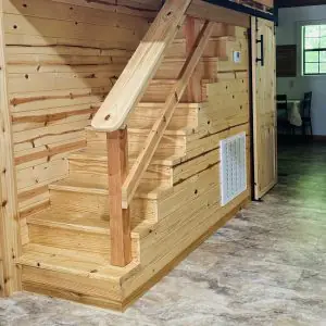 #image_title Wooden staircase to a loft inside a rustic room, with pale wood panel walls and railing.