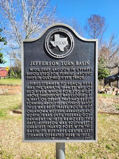 Texas state historical marker titled 'Jefferson Turn Basin' with the Texas seal, describing a wide, deep bayou used for turning ships in the Gulf–Red River trade, set in an outdoor park.
