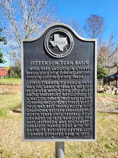 Texas state historical marker titled 'Jefferson Turn Basin' with the Texas seal, describing a wide, deep bayou used for turning ships in the Gulf–Red River trade, set in an outdoor park.