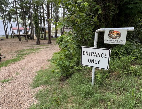 Lakeside trail with trees and a sign reading Canvasback Cove and Entrance Only near the path edge